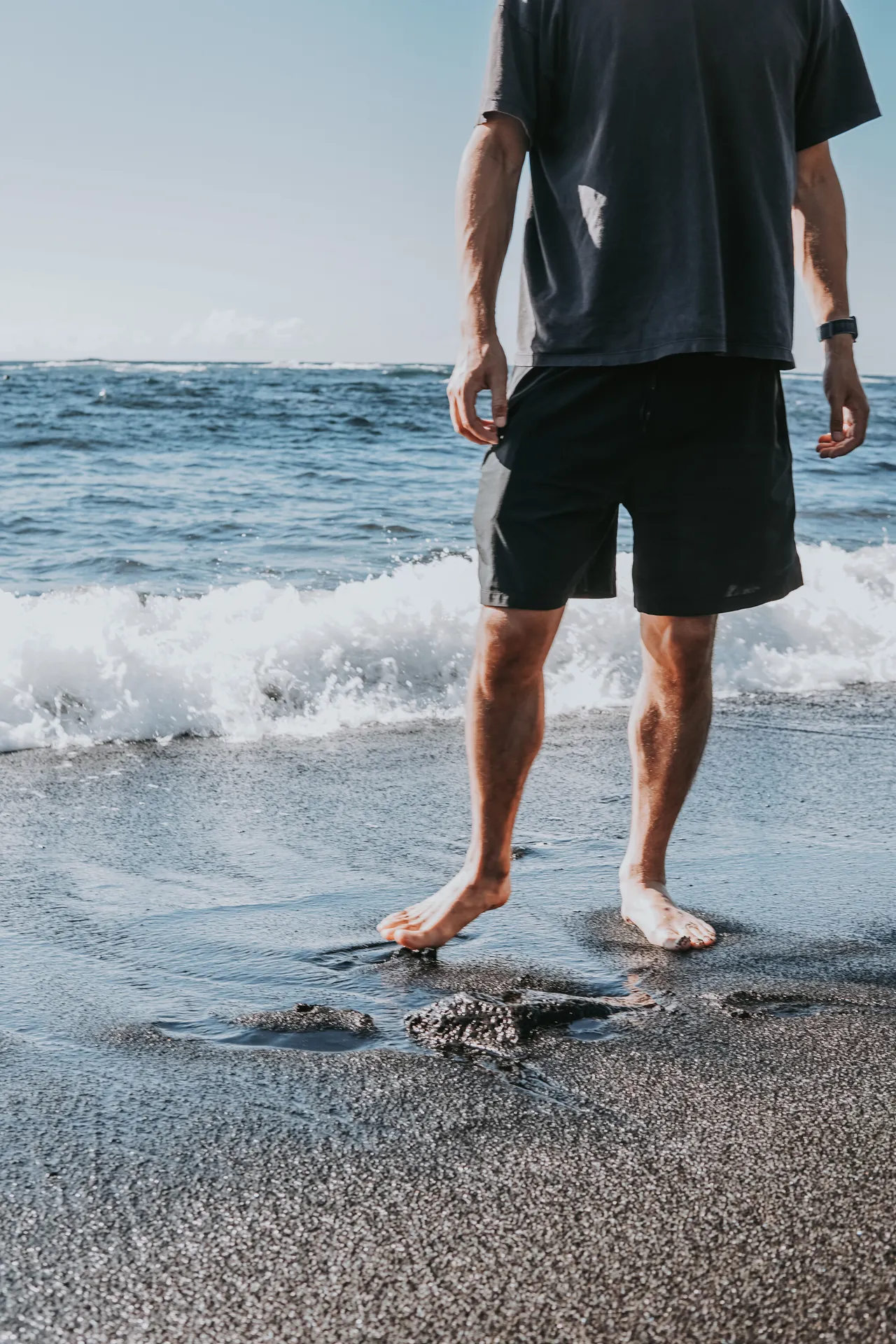 a guy's feet touching the sand at Punalu’u Black Sand Beach
