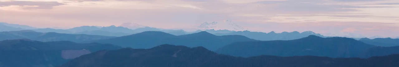 Blue mountain range under a pastel sky with distant snow-capped peaks, creating a serene and peaceful atmosphere. No text visible.
