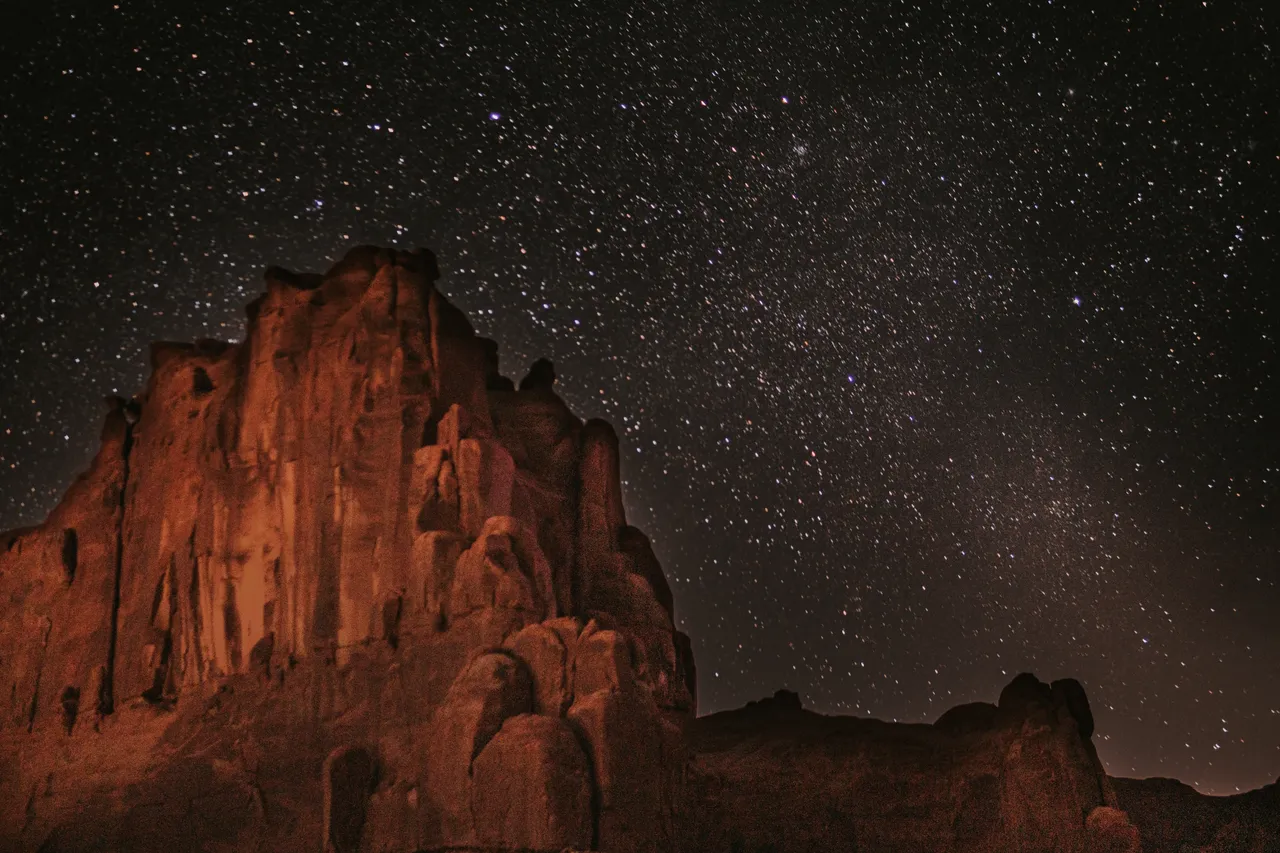 lots of stars scattered above a giant red rock in arches national park