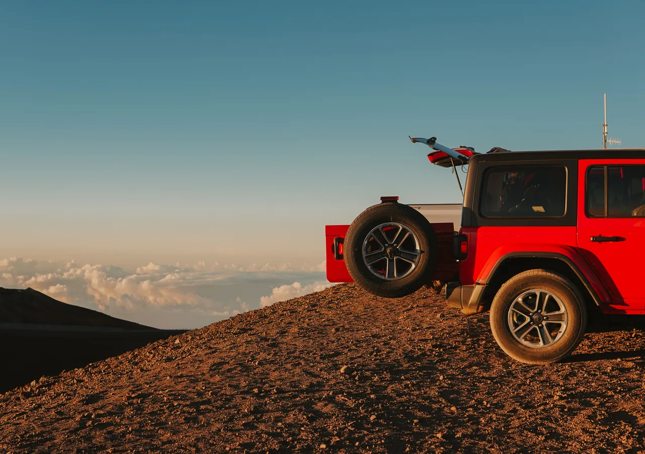 a red jeep with the trunk door opened over looking the mountains at sunset