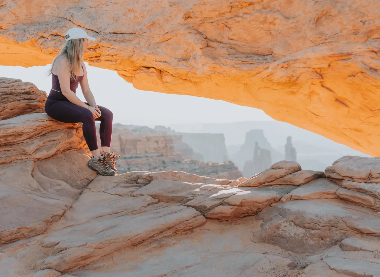 a girl in her purple girlfriend collective workout outfit looking out at the sunrise over the canyonlands national park at mesa arch