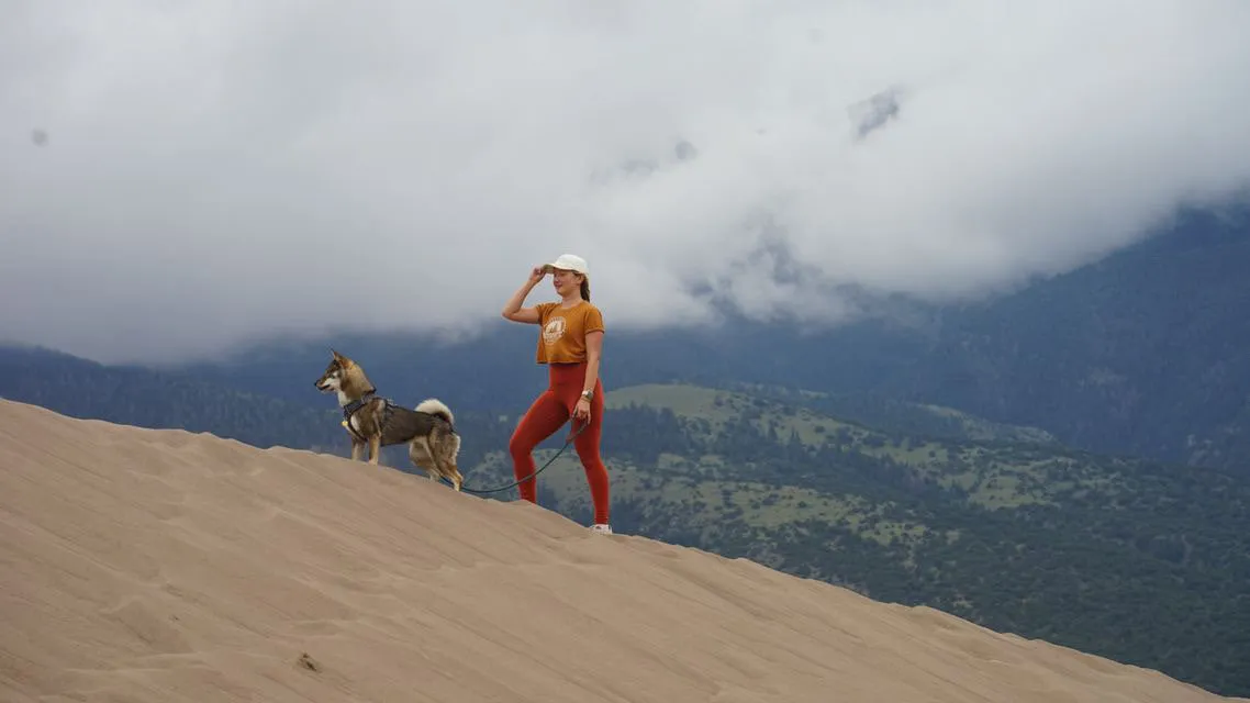 a girl and her dog on the sand dunes in colorado