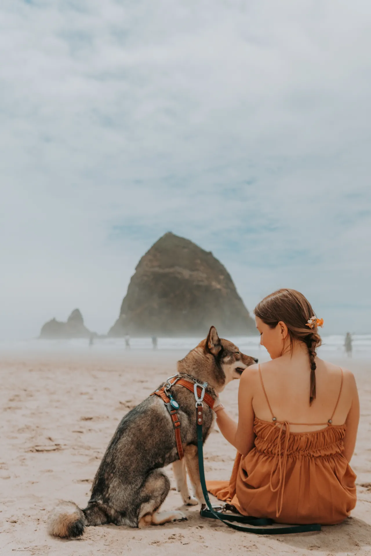 Sitting with Sora at Cannon Beach, warm terracotta tones against misty blues