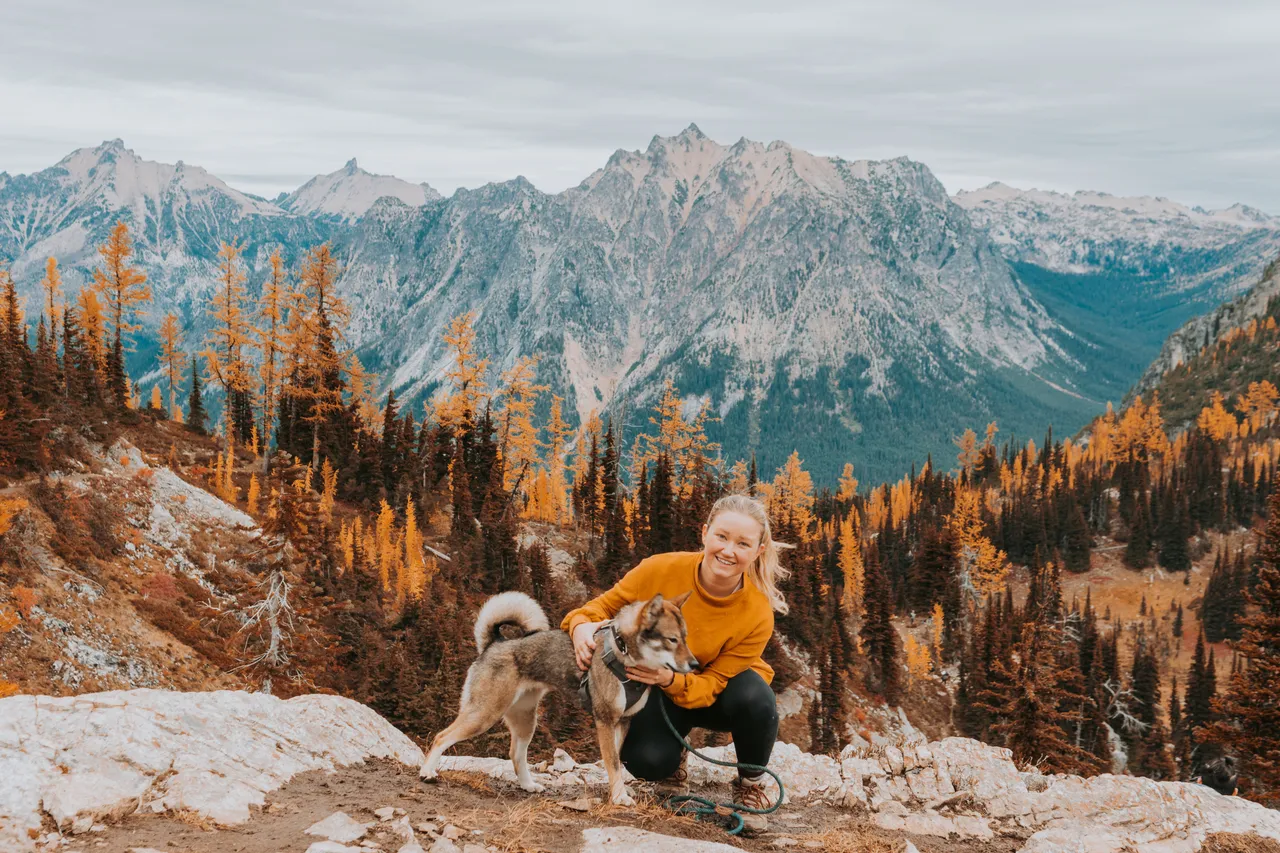 The author and Sora surrounded by golden larches with North Cascades peaks behind them