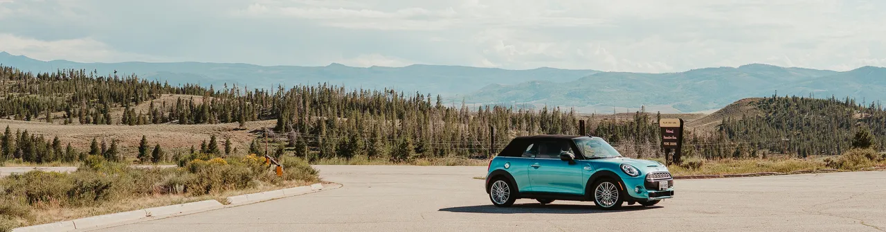 Teal MINI Cooper convertible parked at a mountain overlook in Colorado with sweeping Rocky Mountain views