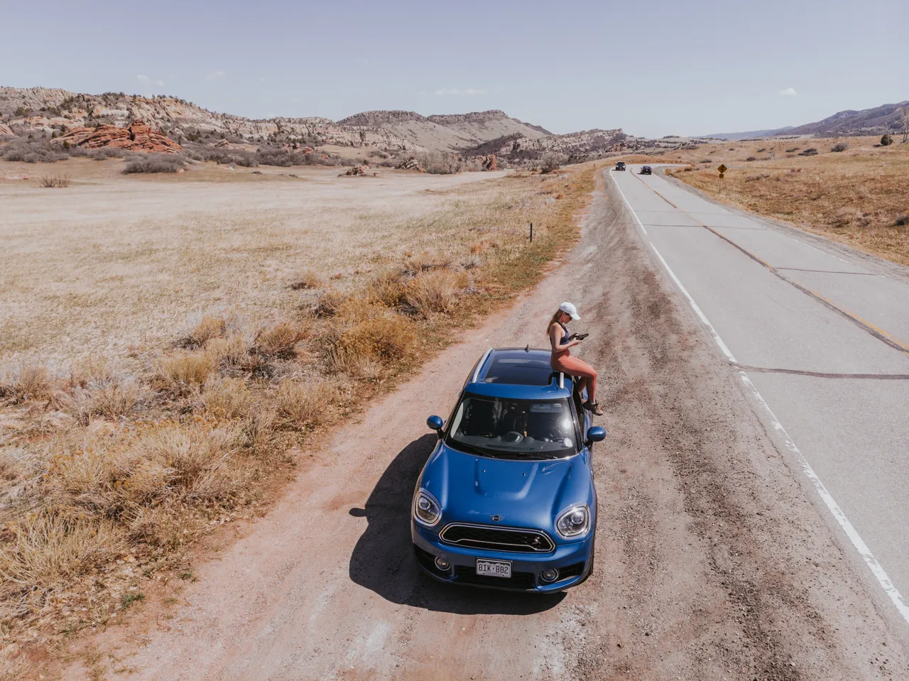 Sitting on the hood of the blue MINI Cooper S Countryman on a dirt road in Colorado, red rock formations in the background