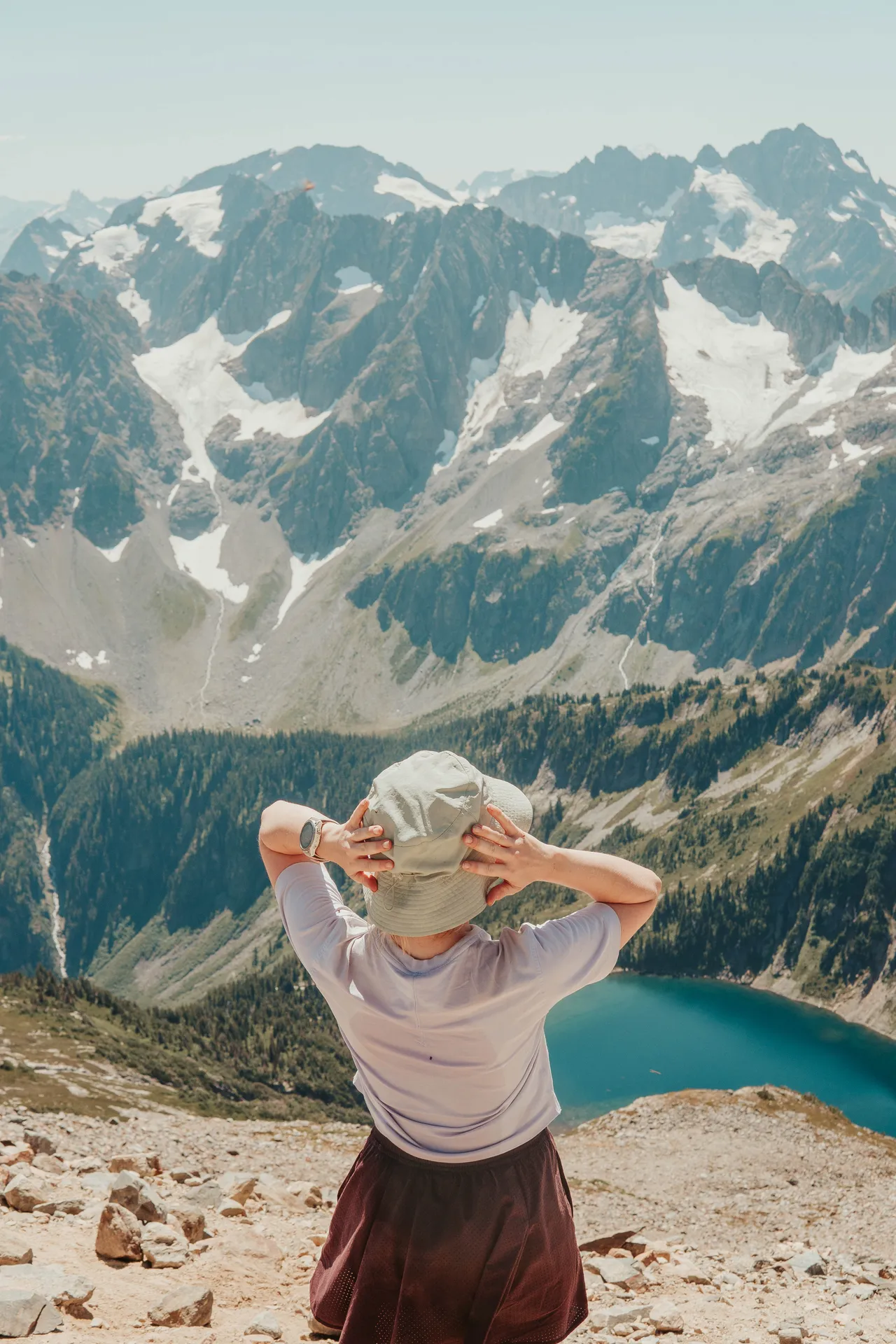 Hiker adjusting bucket hat while looking out over alpine lake and North Cascades mountains