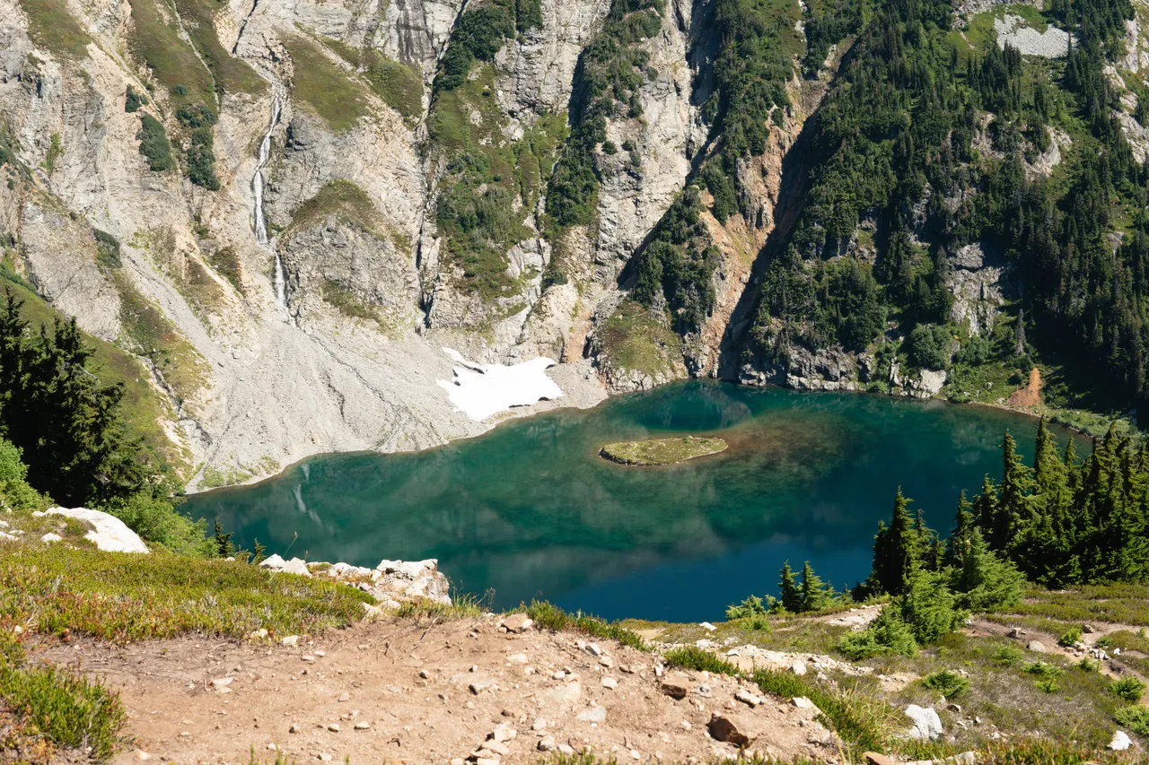 Close-up view of the turquoise alpine lake with a small island, steep rock walls, and a waterfall