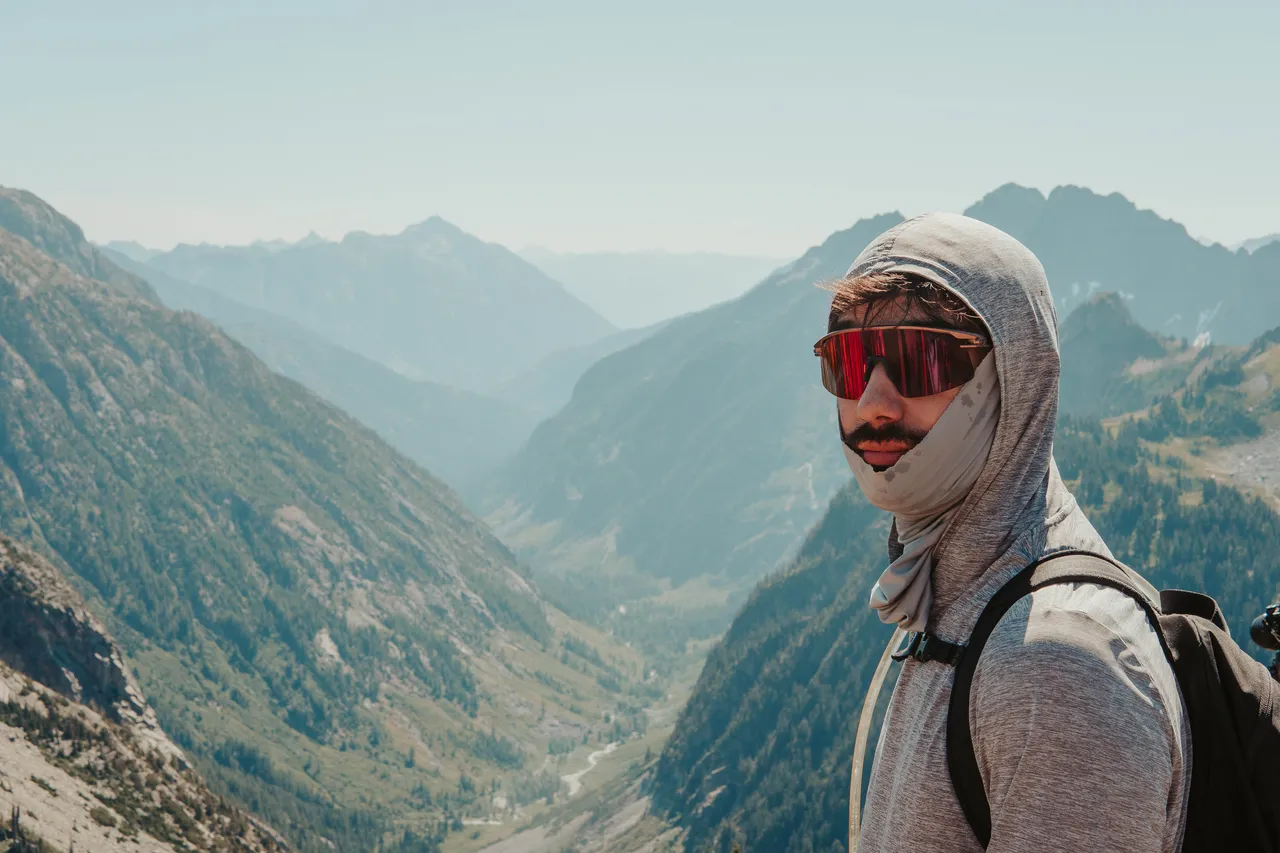 Close-up portrait of a hiker in UPF sun hoodie and red sunglasses with a sweeping Cascade valley behind