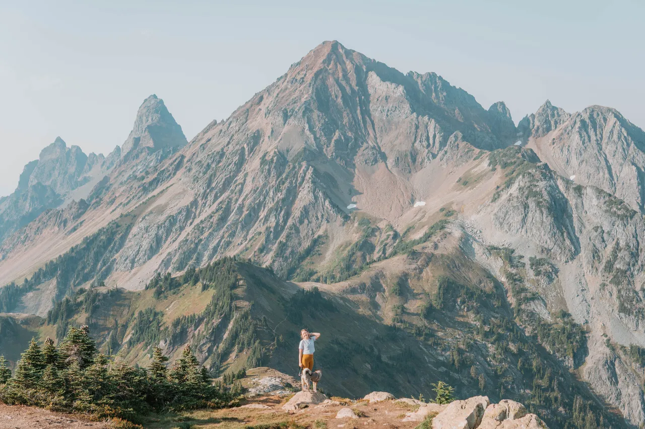 Golden hour view of a woman and dog standing on a ridge at Winchester Mountain with dramatic mountain peaks behind them