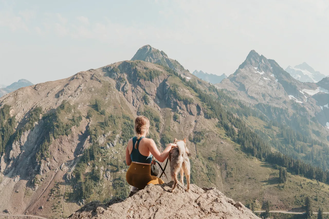Woman sitting with her dog on a rocky overlook at Winchester Mountain with rugged peaks in the background