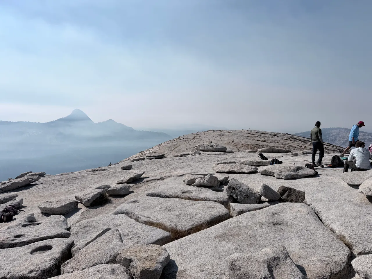 Smoky mountain views beyond the wide granite summit of Half Dome