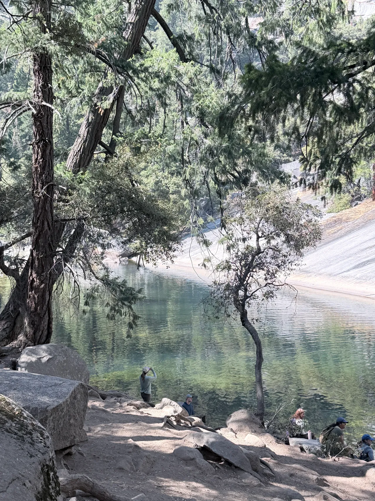 Hikers beside a clear pool beneath Yosemite's granite cliffs