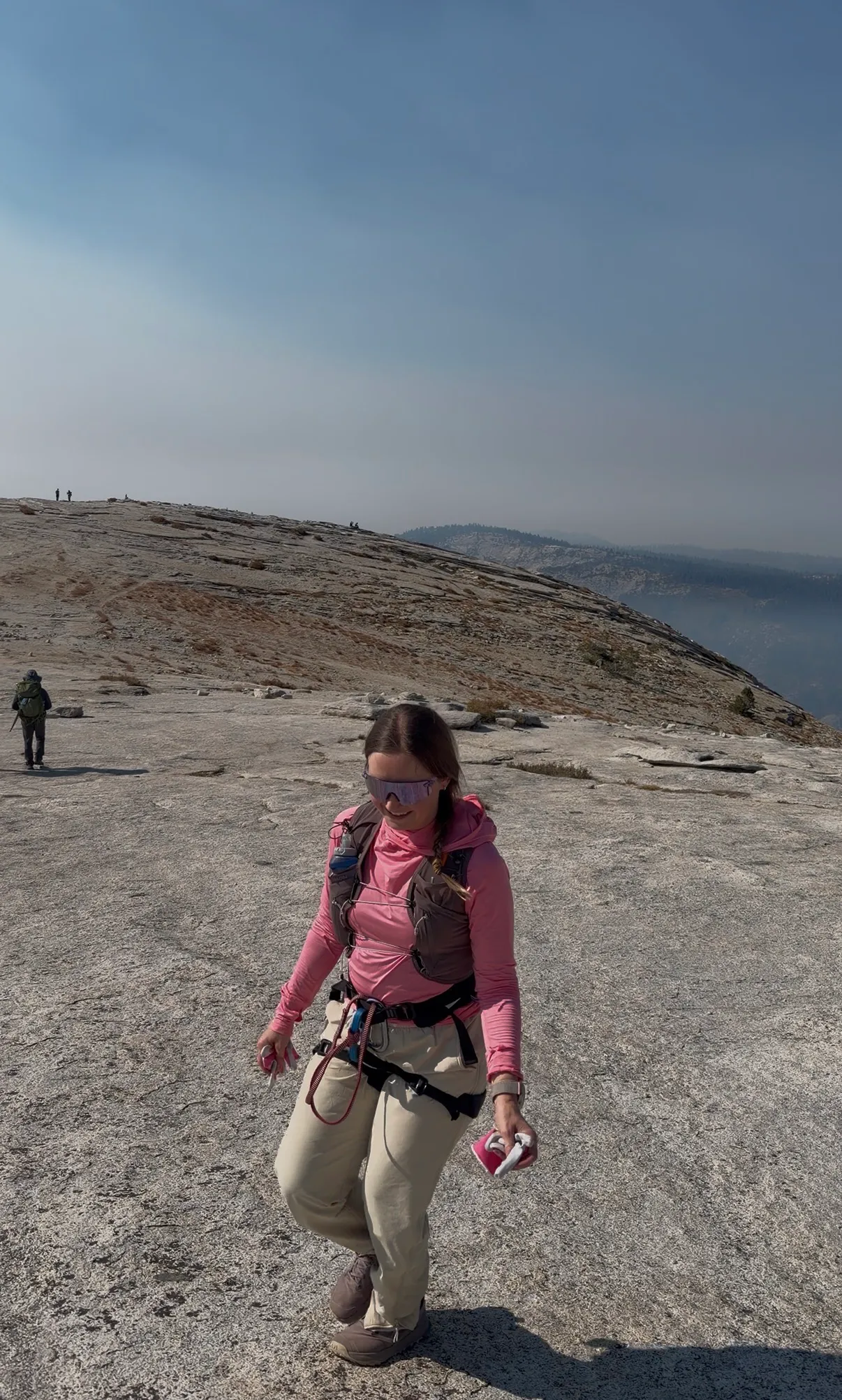 Standing on the broad granite summit of Half Dome in pink hiking clothes